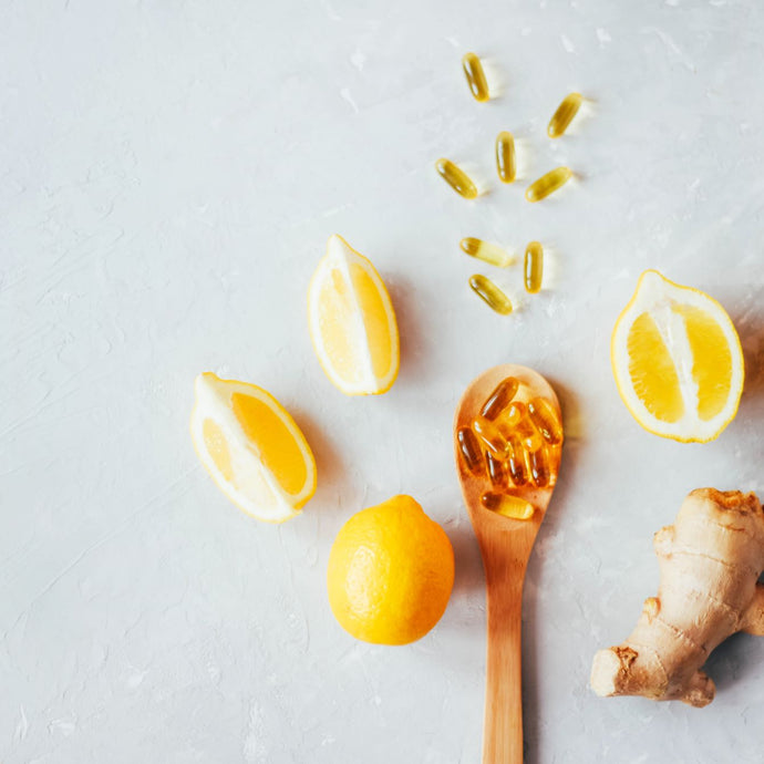 lemons, supplement capsules, ginger root and a wooden spoon with supplement capsules scattered on a countertop