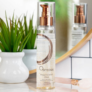 bottle of osmosis elixir displayed on a countertop in a bathrooms with a plant and mirror