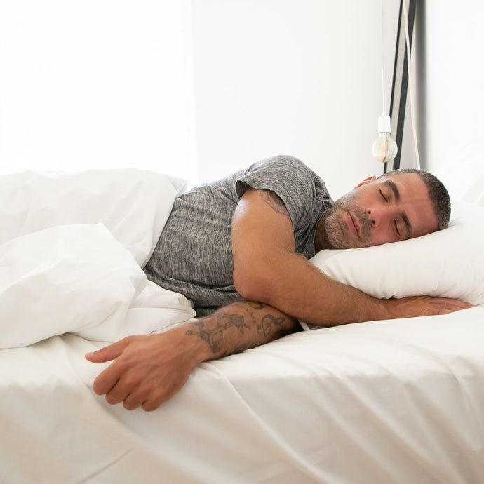 male sunlighten model with tattoos is sleeping on his side in a white bed