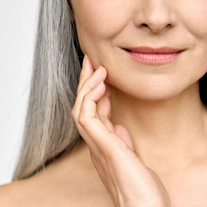 Sunlighten Model with gray hair is touching her youthful skin