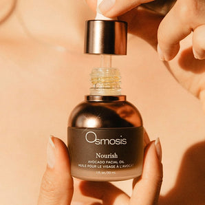 model is holding a bottle of opened osmosis nourish facial oil with her hands
