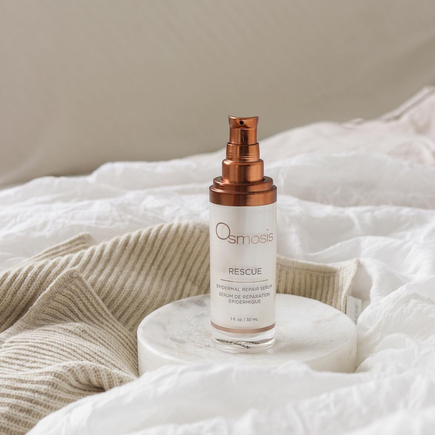 bottle of skincare without cap on displayed on various white linens