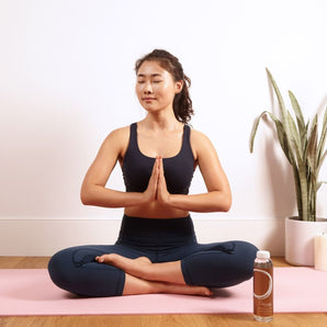 model doing a yoga pose sitting on yoga mat with a bottle of immune defense elixir by osmosis