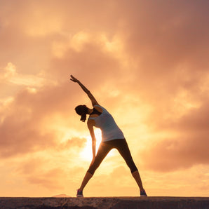 woman stretching outside in work out clothes with sun in front of her