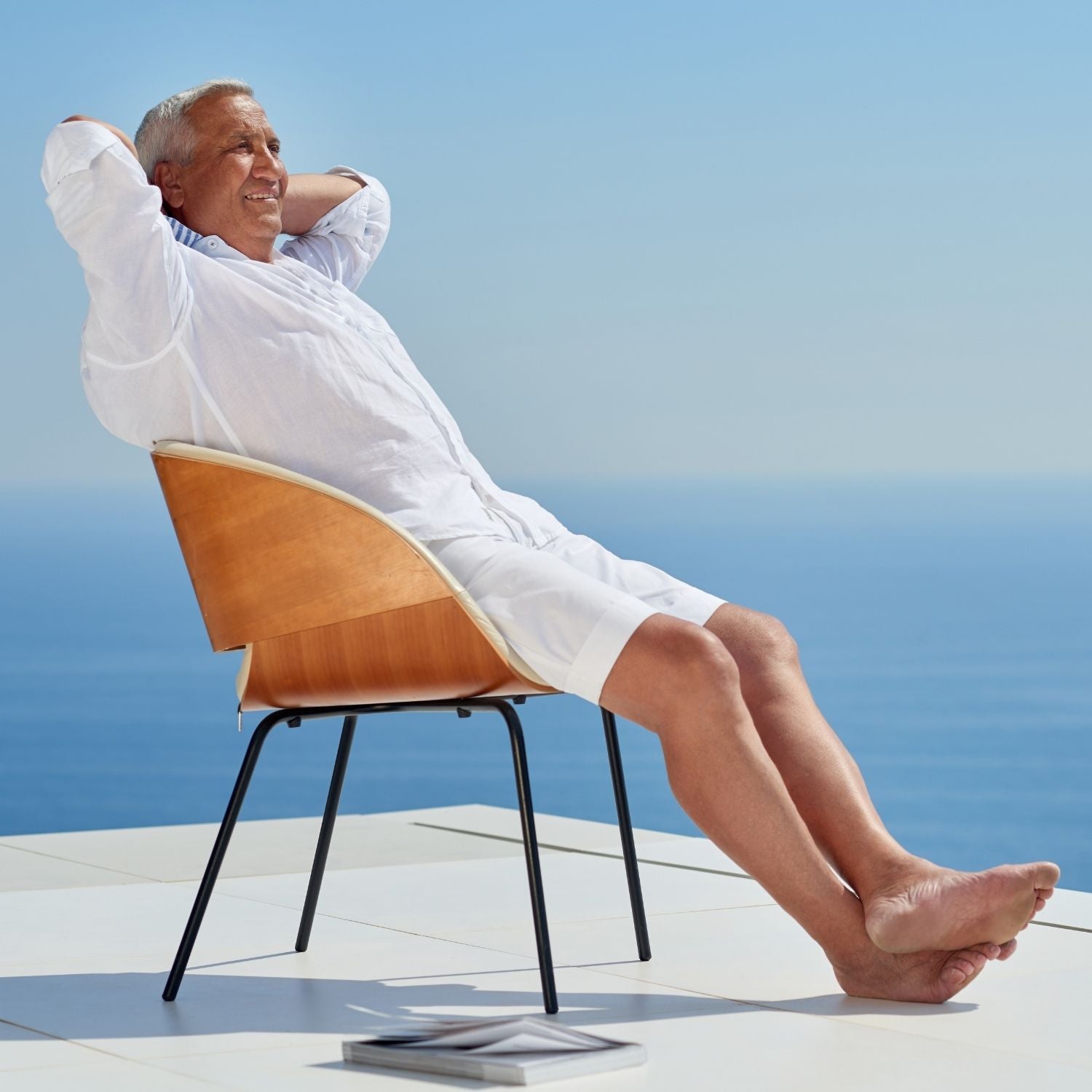 smiling older gentleman in white linen clothes sitting on a deck over looking the ocean