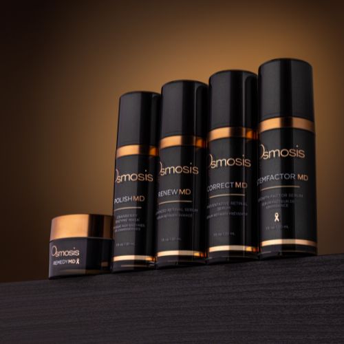 five black and gold bottles of osmosis skincare product lined up in a row displayed on dark wooden shelf
