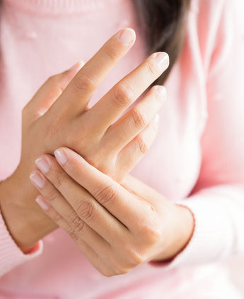 female model in a pink sweater is holding her hands suffering from inflammation 