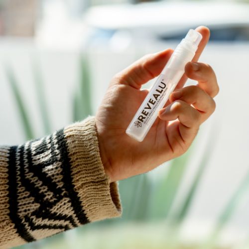 close up of a model's hand holding a tube of face spray by revealu
