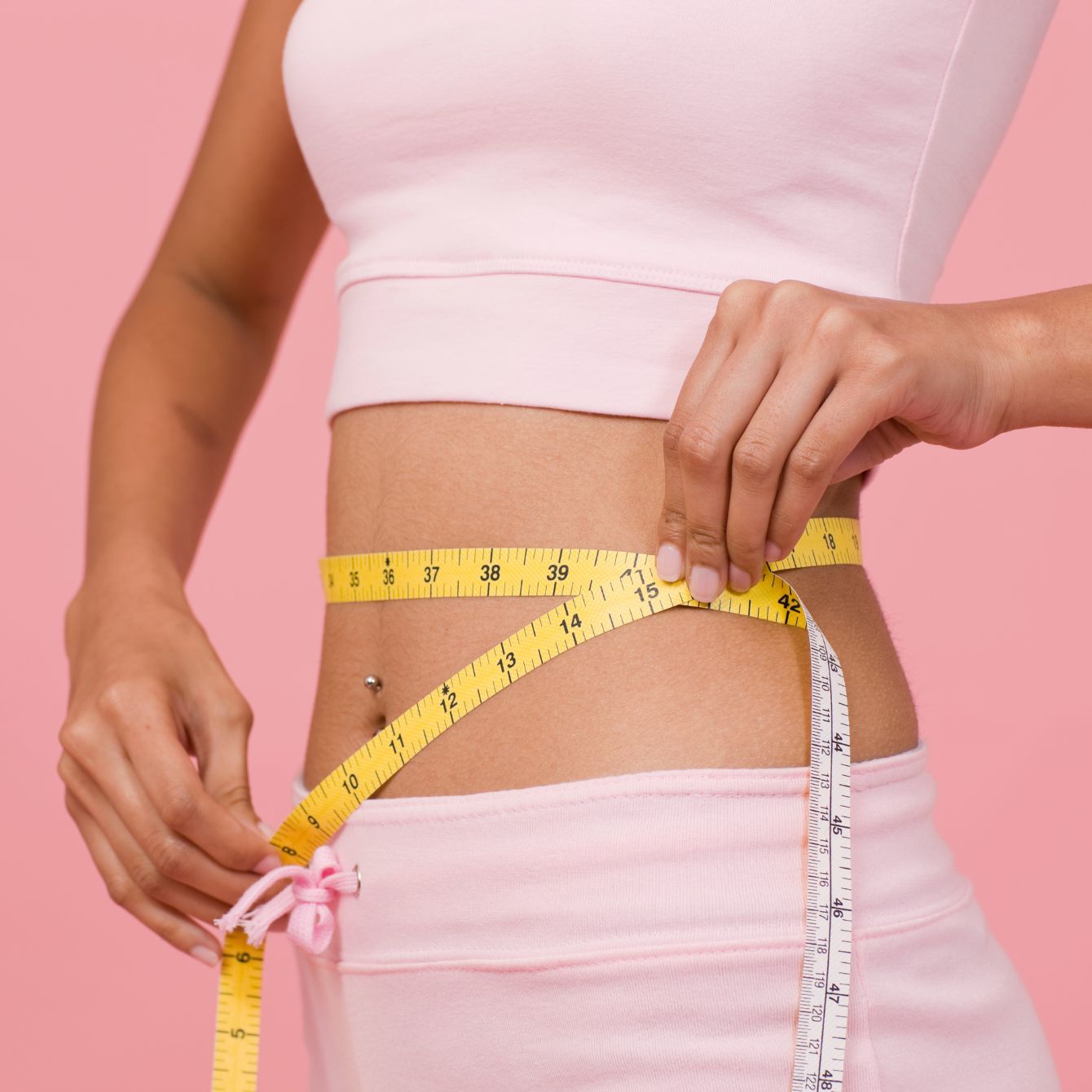 female model in pink is holding a measuring tape around her waste to promote weight loss with prism light pad